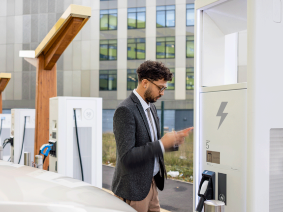 Homme regardent son téléphone portable tout en chargeant son véhicule électrique