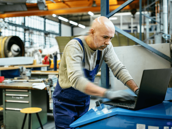 homme en salopette dans une usine, travaillant sur un ordinateur portable