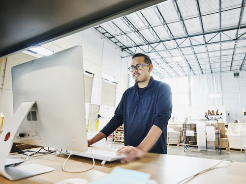 male warehouse worker checking orders at computer workstation